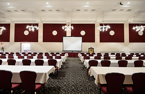 A view of a MSU Union meeting space that has rows of tables with white tablecloths and maroon upholstered chairs.