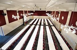 A top down view of a MSU Union meeting space that has rows of tables with white tablecloths and maroon upholstered chairs.