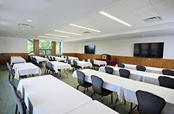 A view of another MSU Union meeting space that has rows of tables with white tablecloths and black chairs, and windows to the left.